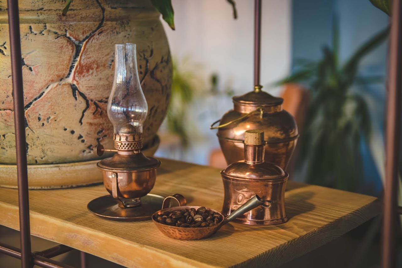 Stylish indoor arrangement with copper vintage items and a large ceramic vase on a wooden shelf.
